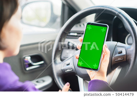 Young female driver using touch screen smartphone in a car. green chroma key on the phone display 50414479
