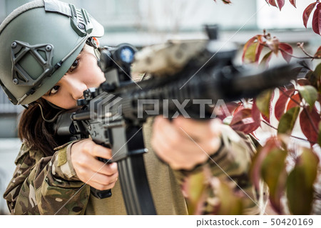 A girl wearing a camouflage uniform playing an survival game with an air gun A girl wearing a camouflage uniform playing an survival game with an air gun 50420169