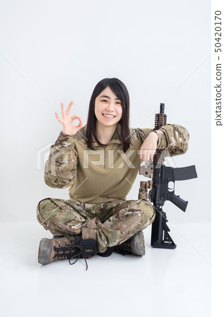 在白色背景上穿著迷彩服裝並且有一把氣槍的女孩也拿著一個圓圈用手指 在白色背景上穿著迷彩服裝並且有一把氣槍的女孩也拿著一個圓圈用手指 50420170
