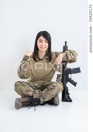 在白色背景上穿著迷彩服裝並且有一把氣槍的女孩也在製作膽量姿勢 在白色背景上穿著迷彩服裝並且有一把氣槍的女孩也在製作膽量姿勢 50420172