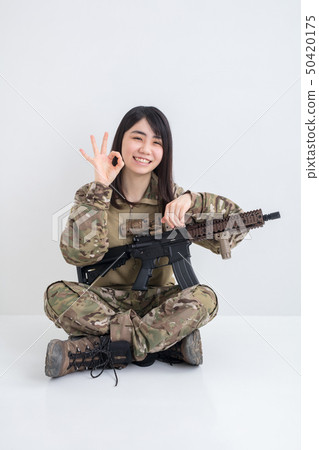 在白色背景上穿著迷彩服裝並且有一把氣槍的女孩也拿著一個圓圈用手指 在白色背景上穿著迷彩服裝並且有一把氣槍的女孩也拿著一個圓圈用手指 50420175