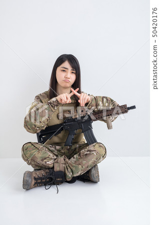 在白色背景上穿著迷彩服裝並且有一把氣槍的女孩也用手指放十字架 在白色背景上穿著迷彩服裝並且有一把氣槍的女孩也用手指放十字架 50420176