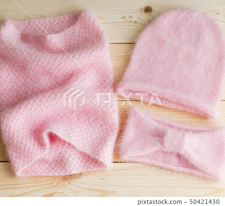 A set of caps, necks and headbands knitted by hand from pink Angora, on wooden background A set of caps, necks and headbands knitted by hand from pink Angora, on wooden background 50421430