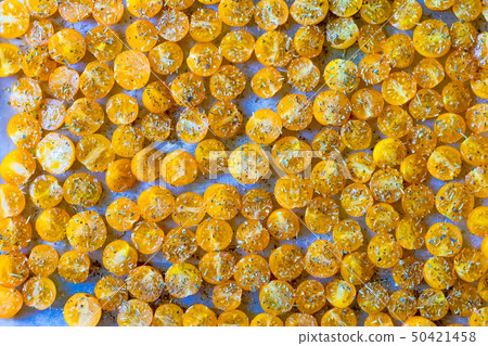 Cut the yellow cherry tomatoes sprinkled with spices on white parchment prepared for drying Cut the yellow cherry tomatoes sprinkled with spices on white parchment prepared for drying 50421458