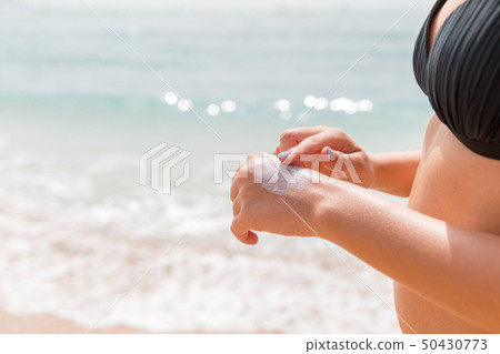 Woman in swimwear is applying sun cream on her Woman in swimwear is applying sun cream on her 50430773