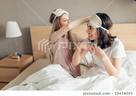 beautiful happy women sitting on bed with eye mask on head 50434093