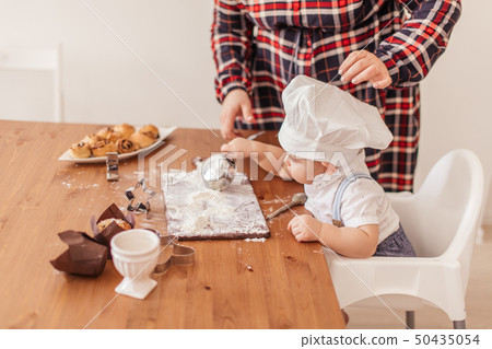 Infant cook baby portrait wearing chef hat playing with dough at kitchen table. 50435054