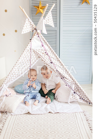 Couple infant boys of 1-year old playing in toy tent with garland at nursery. 50435129