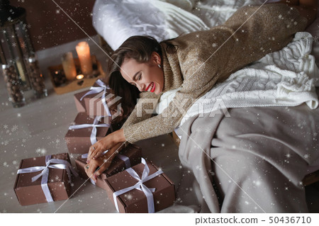 Close up portrait of an excited young woman opening present box while lying in bed at home Close up portrait of an excited young woman opening present box while lying in bed at home 50436710