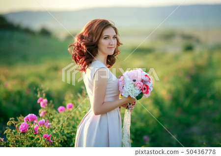 A bride in a white dress holds a bouquet of roses and callas on the background of green grass. A bride in a white dress holds a bouquet of roses and callas on the background of green grass. 50436778