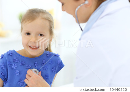 Doctor examining a little girl by stethoscope. Happy smiling child patient at usual medical 50440320