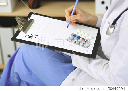 Unknown woman doctor at work at hospital. Pills at medical clipboard. Young female physician write 50440694