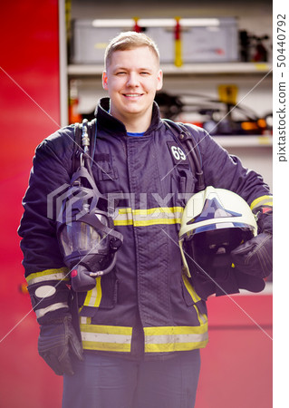 Photo of happy man firefighter with helmet in his hands against background of fire truck 50440792