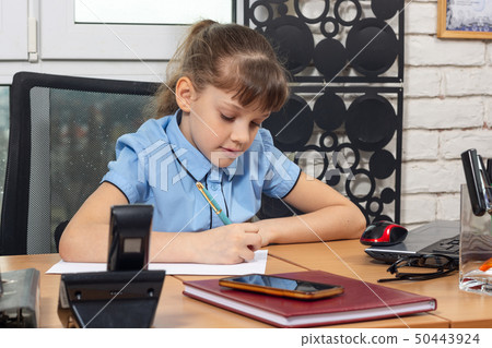 An eight-year girl writes on a sheet of paper at a An eight-year girl writes on a sheet of paper at a 50443924