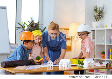 Teacher helping pupils in helmets making construction sketches Teacher helping pupils in helmets making construction sketches 50444119