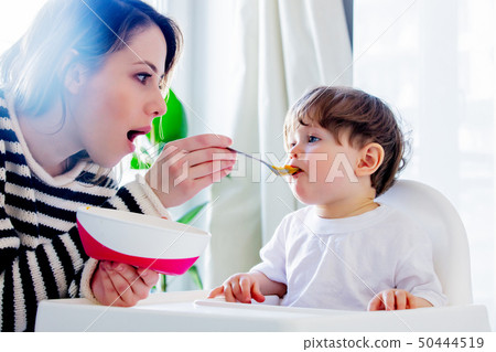 mother try to feeding a toddler boy with a spoon in a chair mother try to feeding a toddler boy with a spoon in a chair 50444519