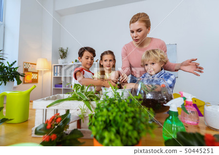 Three pupils and their teacher standing near table with plants 50445251