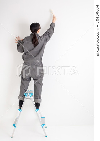 Girl in a workwear with a white background paints a wall on a wall DIY 50450634