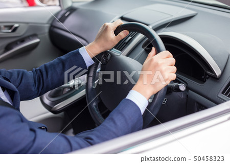 A man driving a car while a man in a suit at work is driving 50458323