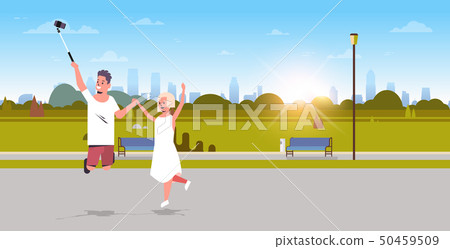 young couple using selfie stick taking photo on smartphone camera man woman jumping having fun city young couple using selfie stick taking photo on smartphone camera man woman jumping having fun city 50459509