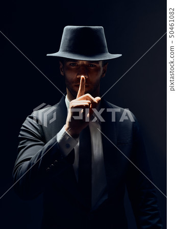 Serious man in black suit and hat keeps finger on 50461082