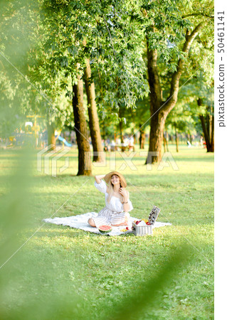 Young european woman in hat resting on plaid with fruits in park. Young european woman in hat resting on plaid with fruits in park. 50461141