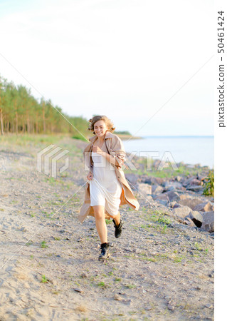 Young pretty woman walking on shingle beach and wearing summer coat. Young pretty woman walking on shingle beach and wearing summer coat. 50461424