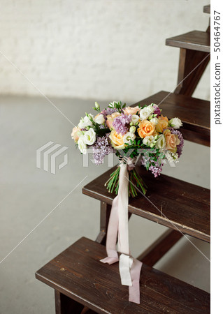 Beautiful bouquet of flowers of roses and lilac stands on a wooden ladder against a white brick wall 50464767