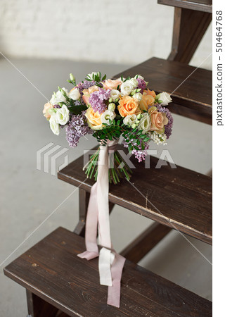 Beautiful bouquet of flowers of roses and lilac stands on a wooden ladder against a white brick wall 50464768