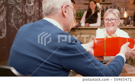 Senior man giving her wife an retirement gift during dinner in a restaurant 50465471
