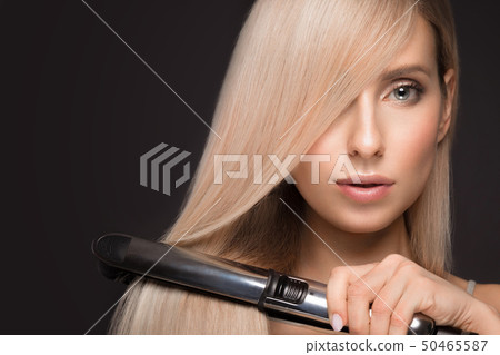 Beautiful blond girl with a perfectly smooth hair, classic make-up with curling styler in the hands. Beautiful blond girl with a perfectly smooth hair, classic make-up with curling styler in the hands. 50465587
