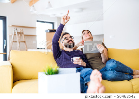 A young couple with tablet sitting on sofa, moving in new home. 50468542