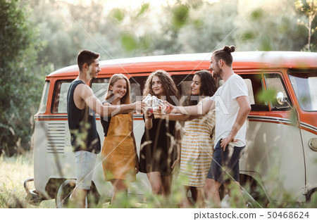 A group of friends standing outdoors on a roadtrip through countryside, clinking bottles. A group of friends standing outdoors on a roadtrip through countryside, clinking bottles. 50468624