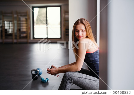 A young girl or woman with earphones and smartphone in a gym. A young girl or woman with earphones and smartphone in a gym. 50468823