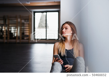 A young girl or woman with earphones and smartphone in a gym. 50468832