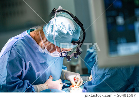 Surgeon and his assistant performing cosmetic surgery in hospital operating room. Surgeon in mask 50491597
