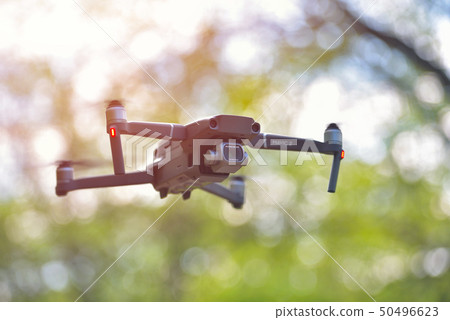 Flying drone with camera hovering inside a forrest Flying drone with camera hovering inside a forrest 50496623