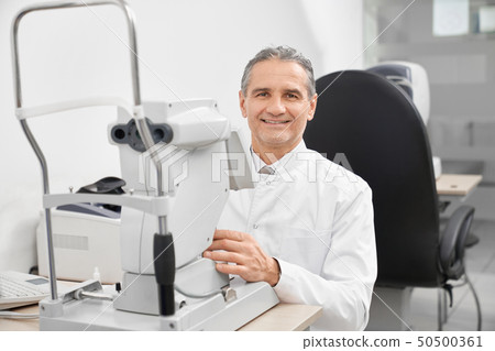 Doctor smiling, posing with modern eye test machine. Doctor smiling, posing with modern eye test machine. 50500361