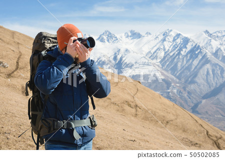 Portrait of a bearded male photographer in sunglasses and a warm jacket with a backpack on his back Portrait of a bearded male photographer in sunglasses and a warm jacket with a backpack on his back 50502085
