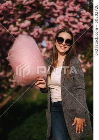 Close up portrait of smiling girl holding cotton candy in hands. Girl dressed in grrey blazer and 50502726