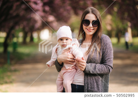 Beautiful mom walk with her baby girl on hands in the park. Pink background Beautiful mom walk with her baby girl on hands in the park. Pink background 50502995