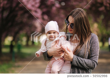 Beautiful mom walk with her baby girl on hands in the park. Pink background Beautiful mom walk with her baby girl on hands in the park. Pink background 50502998