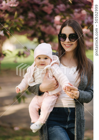 Beautiful mom walk with her baby girl on hands in the park. Pink background 50502999