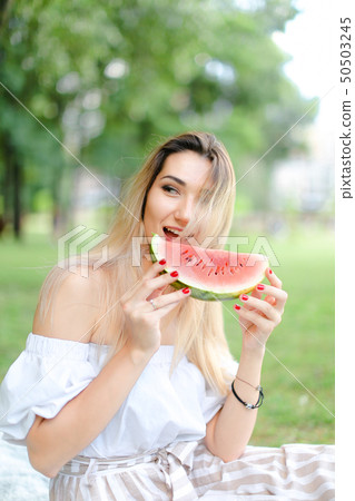 Young european girl eating watermelon and wearing dress, grass in background. Young european girl eating watermelon and wearing dress, grass in background. 50503245