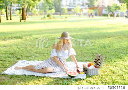 Young beautiful gitrl sitting in park on plaid near fruits, grass in background. Young beautiful gitrl sitting in park on plaid near fruits, grass in background. 50503516