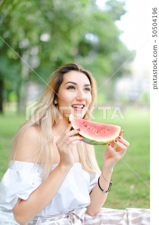 Young woman eating watermelon and wearing dress, grass in background. 50504196