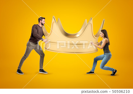 Side view of man and woman, both in casual clothes, carrying enormous gold crown on yellow 50506210