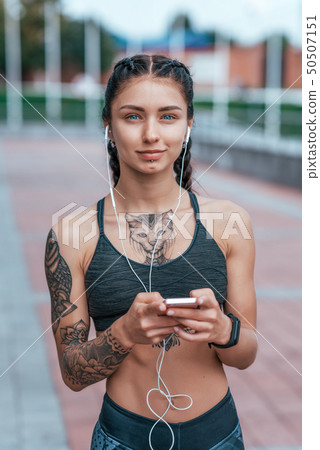 Beautiful woman smiling, happy girl in summer in city, tanned skin tattoo. Sportswear top. Phone Beautiful woman smiling, happy girl in summer in city, tanned skin tattoo. Sportswear top. Phone 50507151