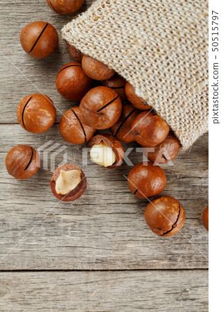 Macadamia nuts spilled out of the bag on a wooden 50515797