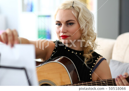 Mature blond woman turning notes pages while playing western acoustic guitar 50518066